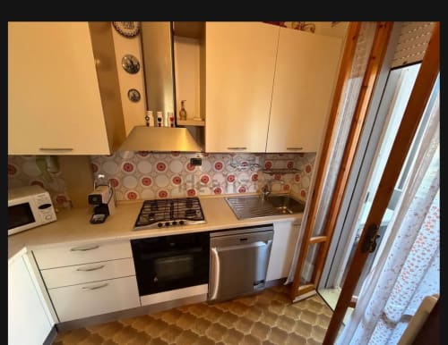 Cucina moderna nell'appartamento di Cervia con mobili bianchi, piano cottura a gas, elettrodomestici in acciaio inox e rivestimento rosso decorativo