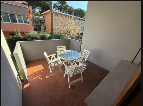 Patio privato con tavolo rotondo blu e sedie bianche a Romagnapartments a Cervia, circondato da muri bianchi e giardino