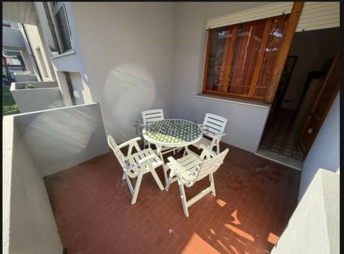 Area salotto privata con sedie bianche e tavolo rotondo su pavimento in cotto presso Romagnapartments a Cervia