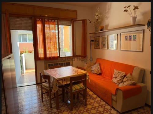 Luminoso salotto a Cervia con divano arancione, tavolo da pranzo e accesso al balcone con vista sul giardino