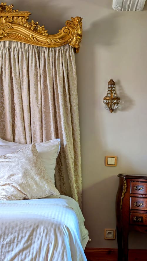 Elegant bedroom at Domaine Au Fil Du Temps with gold-trimmed canopy bed, cream curtains, and ornate wall sconce