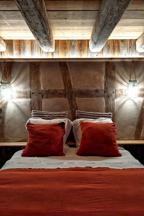 Rustikales Schlafzimmer im Domaine Au Fil Du Temps mit Holzbalken, weißer Bettwäsche, roten Kissen und hängenden Laternen