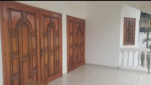 Hall d'entrée de la Villa des Pins Toscane avec portes sculptées en bois et carrelage blanc à Libreville