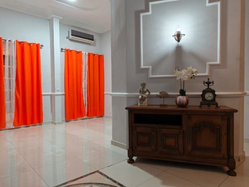Intérieur élégant de La Villa des Pins avec commode en bois foncé, objets de décoration et rideaux orange vibrants