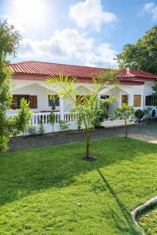 Villa La Villa des Pins Toscane à Libreville : façade blanche, toiture rouge et jardin luxuriant