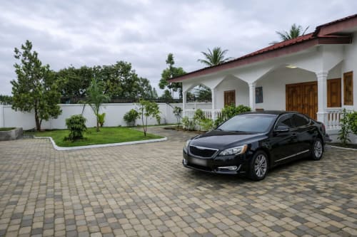 Berline noire garée à l'entrée de la villa La Villa des Pins à Libreville, avec son architecture aux murs blancs et ses jardins entretenus