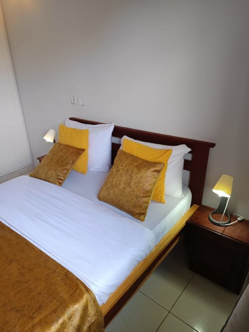Chambre villa Toscane à La Villa des Pins, Libreville avec lit king-size, oreillers dorés et lampe de chevet