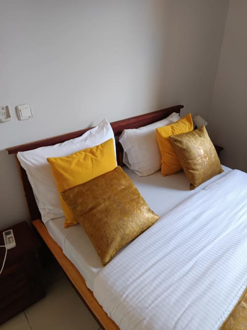 Chambre élégante de La Villa des Pins avec coussins de décoration dorés et jaunes sur lit en bois à Libreville