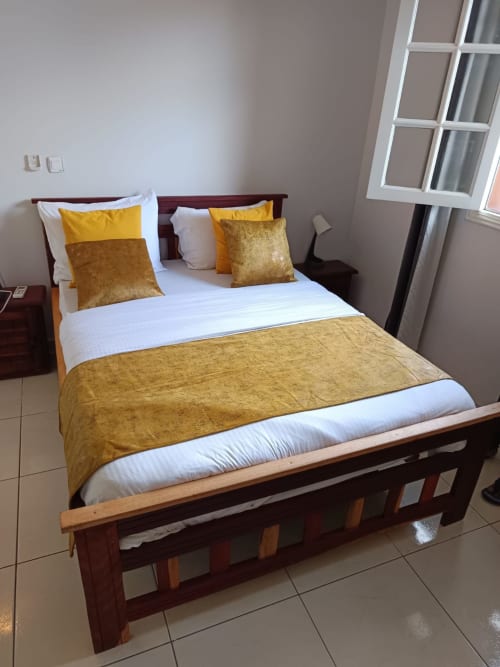 Chambre Toscane de la Villa des Pins à Libreville : lit queen-size, literie dorée, cadre en bois et vue sur le jardin