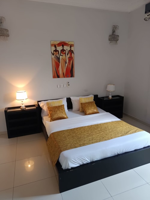 Chambre de luxe à La Villa des Pins à Libreville : lit noir, accents dorés et œuvres d'art africaines