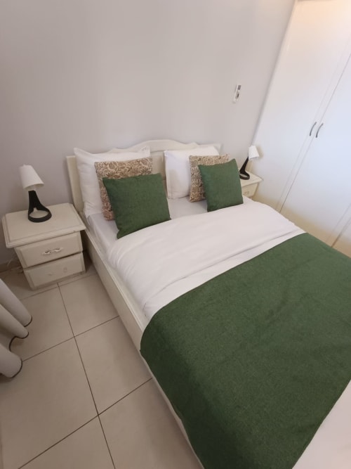 Chambre moderne de la villa La Villa des Pins à Libreville avec linge de lit vert, draps blancs et tables de nuit crème