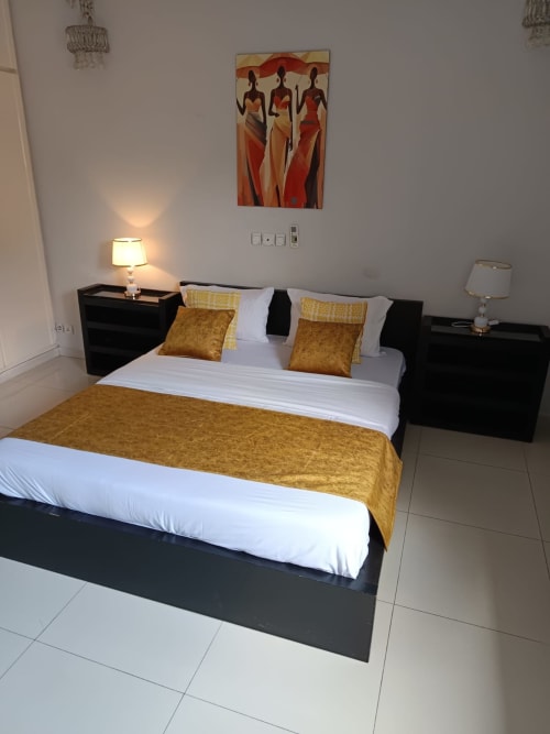Chambre spacieuse de la villa La Villa des Pins à Libreville avec accents dorés, mobilier noir moderne et inspirations africaines