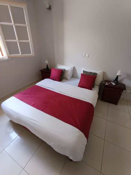 Chambre moderne de la Villa des Pins à Libreville avec literie blanche, accents rouges et vue sur le jardin