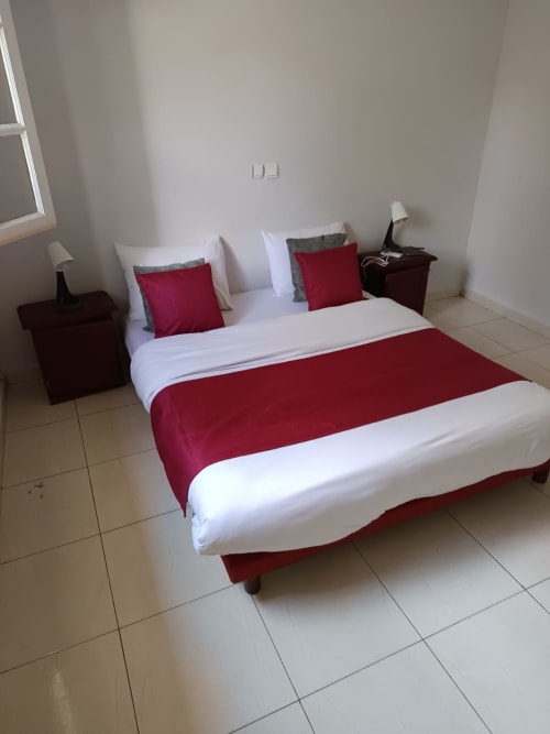 Chambre de style toscan à La Villa des Pins, Libreville, avec chemin de lit rouge, draps blancs et vue sur le jardin