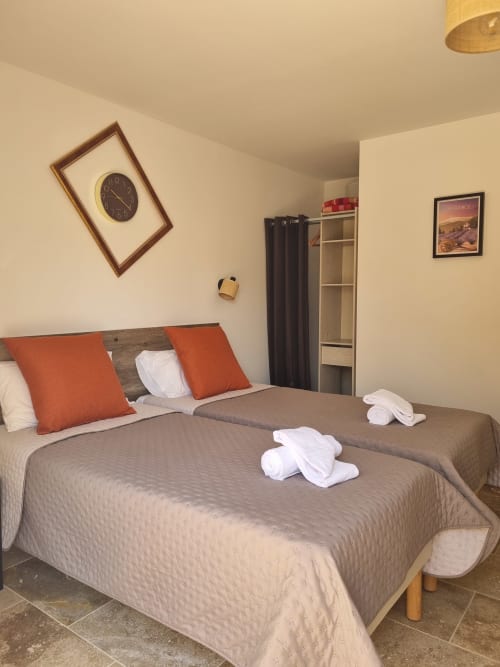 Chambre douillette à L'Orée du Ventoux avec lit double, oreillers orange et horloge à Crillon-le-Brave
