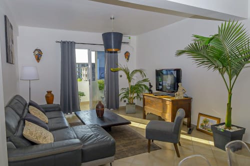 Séjour moderne à l'appartement La Villa des Pins à Libreville avec canapé cuir, mobilier bois, télévision et plantes luxuriantes