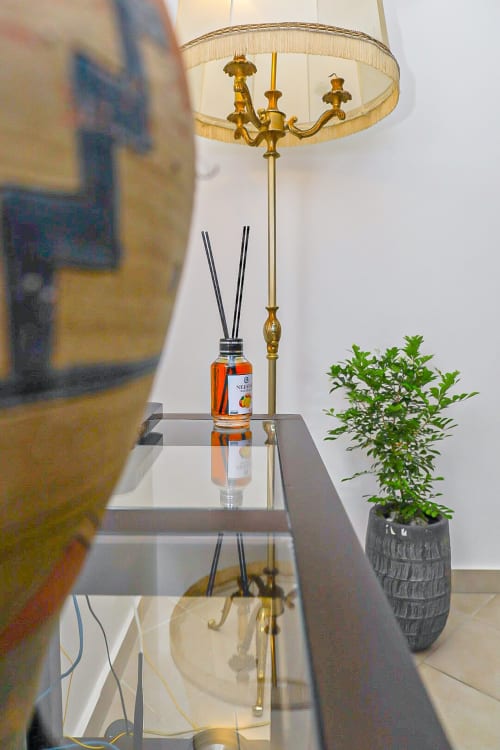 Élégante lampe de table en laiton avec abat-jour crème, diffuseur en carafe et plante en pot sur table d'appoint à La Villa des Pins