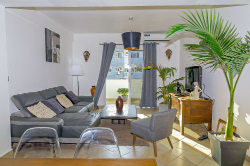 Salon moderne de La Villa des Pins Libreville avec canapé gris, fauteuil, bureau en bois, plante en pot et jardin