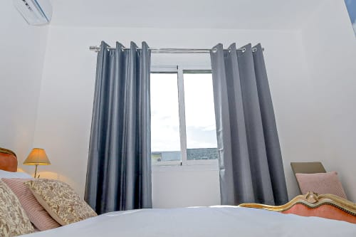 Chambre avec rideaux gris à œillets, murs blancs et vue sur balcon à l'appartement La Villa des Pins à Libreville