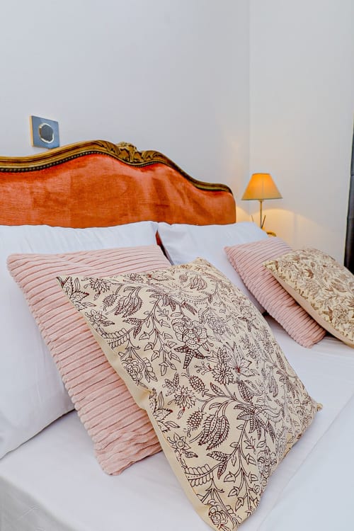 Chambre élégante à La Villa des Pins avec tête de lit en bois ornée, coussins décoratifs et lampe de chevet chaleureuse
