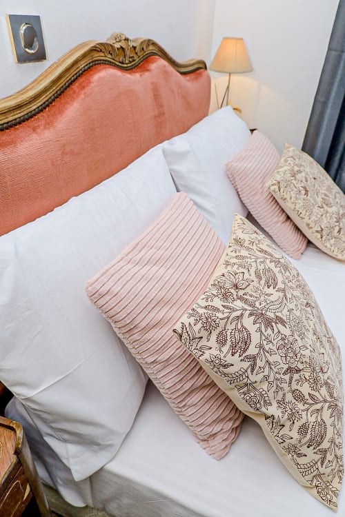 Lit élégant avec tête de lit en corail, linge blanc et oreillers plissés rose pastel à La Villa des Pins