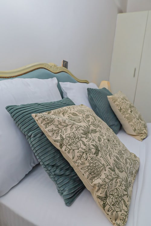 Lit élégamment aménagé avec jeté vert côtelé, coussins floraux décoratifs et draps blancs à La Villa des Pins