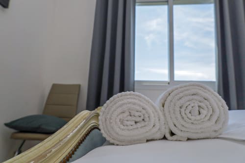 Deux serviettes beige roulées sur un lit à La Villa des Pins avec vue sur le jardin et la fenêtre à Libreville