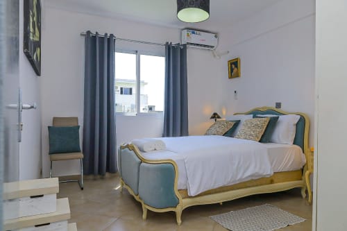 Chambre élégante avec lit doré, linge blanc, oreillers verts et équipements modernes à La Villa des Pins à Libreville
