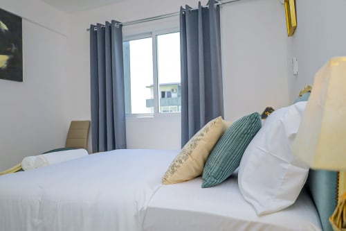 Chambre lumineuse à La Villa des Pins avec literie blanche, coussins décor, rideaux gris et balcon vue jardin