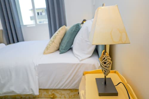 Chambre à La Villa des Pins avec lampe crème sur la table de nuit, coussins décorés et rideaux donnant sur le jardin à Libreville