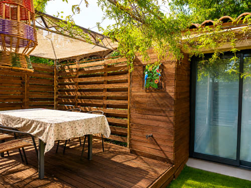Terraza privada de madera con mesa de comedor, pérgola y exuberante vegetación en la casa rural Maison D'hôtes Coeur D'hérault en Péret