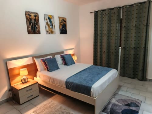 Chambre moderne à La Villa des Pins, Akanda avec accents bleus, éclairage ambiant, œuvres animalières et rideaux verts