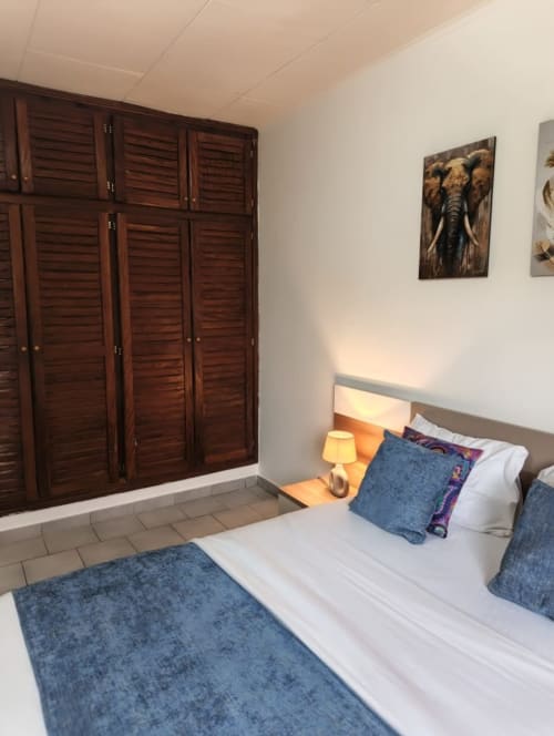 Chambre de La Villa des Pins à Akanda avec armoire à jalousies, literie blanche, accents bleus et décoration d'éléphants