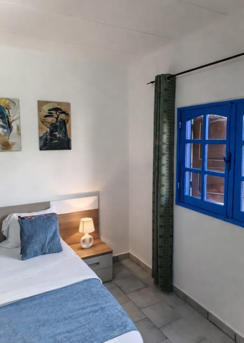 Chambre moderne à La Villa des Pins à Akanda avec baie vitrée bleue, lampe de chevet en bois et œuvre d'art