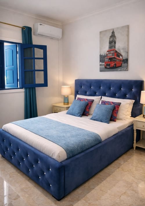 Lit luxueux en velours bleu marine avec literie blanche et coussins décoratifs à La Villa des Pins à Akanda