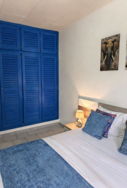 Chambre moderne à La Villa des Pins avec armoire à jalousies bleues, lit blanc aux accents bleus et œuvre d'art éléphant