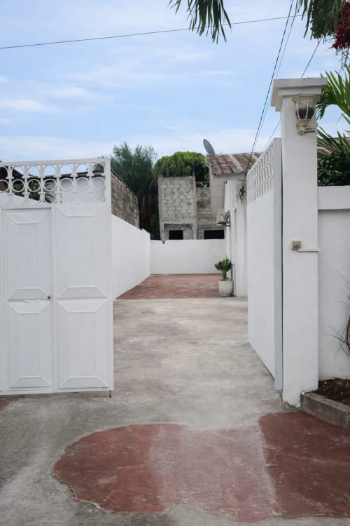 Portail d'entrée de la villa La Villa des Pins à Akanda avec murs blancs et cour en briques