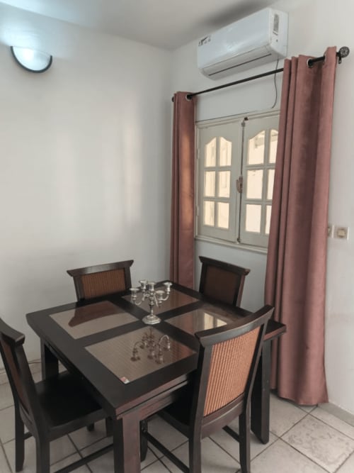 Salle à manger avec table en bois foncé, quatre chaises et chandelier dans l'appartement La Villa des Pins à Akanda, rideaux roses