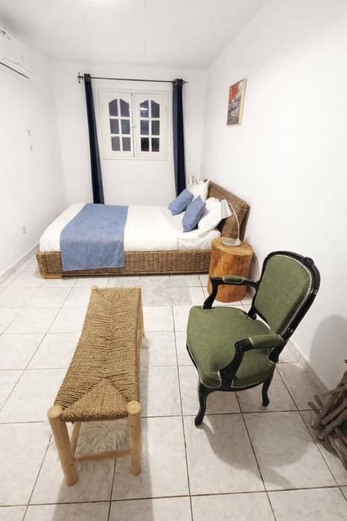 Chambre accueillante à La Villa des Pins à Akanda avec lit en osier, fauteuil vert et portes-fenêtres