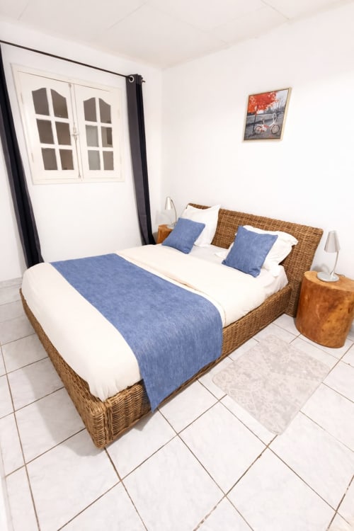 Lit en rotin avec accents bleus dans la chambre lumineuse de La Villa des Pins, Akanda