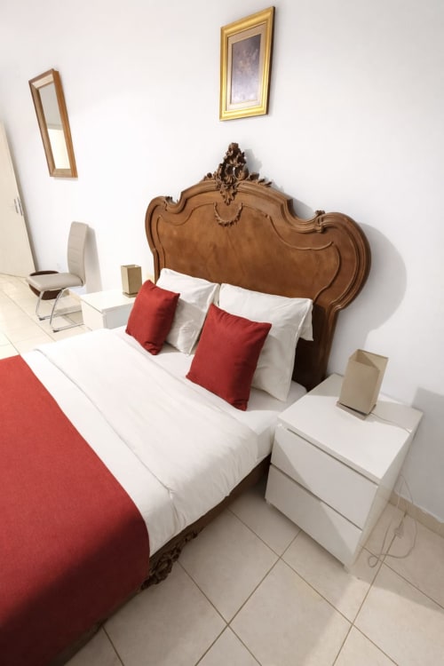 Chambre luxueuse à La Villa des Pins à Akanda avec tête de lit en bois travaillé, oreillers rouges et blancs, literie blanche
