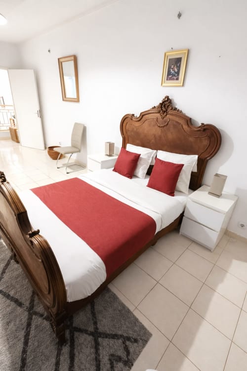Chambre élégante à La Villa des Pins avec lit en bois ouvragé, accents rouges, draps blancs et mobilier moderne à Akanda