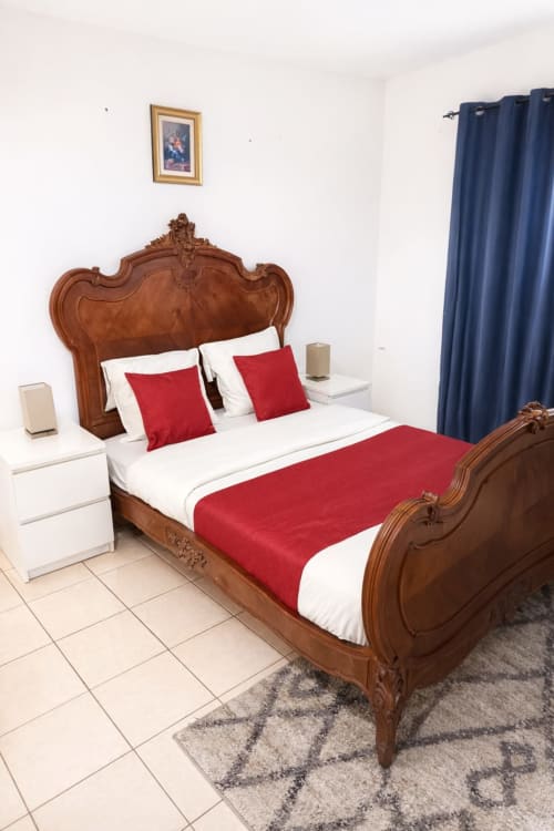 Chambre élégante à La Villa des Pins avec lit en bois orné, literie rouge et blanche, tables de nuit blanches, rideaux bleus
