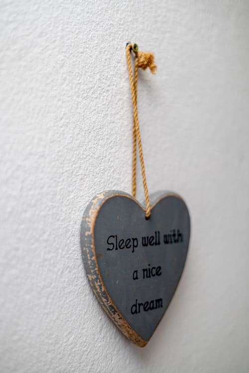Ornement en ardoise en forme de cœur avec le message « Dors bien et fais de beaux rêves » suspendu au mur blanc de l'appartement La Villa des Pins