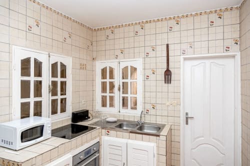 Cuisine entièrement équipée à La Villa des Pins : armoires blanches, crédence carrelée, cuisinière, évier et micro-ondes