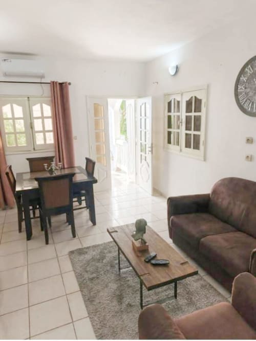 Séjour lumineux à La Villa des Pins à Akanda avec canapé en cuir marron, table à manger et portes vitrées donnant sur
