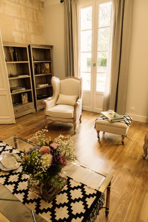 Elegant living room at Château Alto Cormeil with cream armchair, wooden shelving, and black-patterned rug in Saint-Émilion