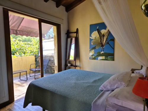 Dormitorio luminoso en Aldea Rural Pazos De Arenteiro con cama azul, paredes amarillas, obras de arte y acceso a terraza