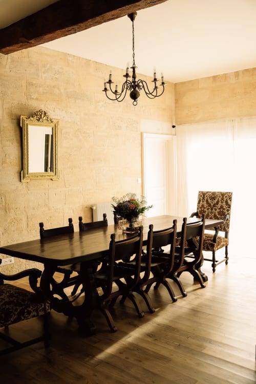 Elegante comedor del Château Alto Cormeil, Saint-Émilion con mesa negra, araña ornamental y paredes de piedra