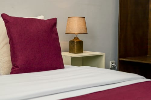 Chambre confortable à La Villa des Pins avec coussin bordeaux, literie blanche et lampe de table en laiton